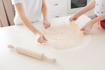 Children's hands roll out the pizza dough on a white table. Having fun together in the kitchen. View from above.