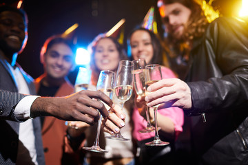 Focus on full champagne flutes in hands of friends standing in row, they toasting with glasses together