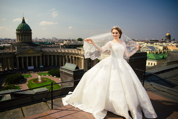 Fototapeta premium Beautiful Bride in a white Wedding Dress outdoors with a Bouquet of flowers and a veil