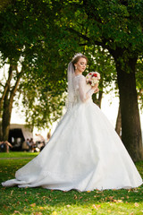 Obraz na płótnie Canvas Beautiful Bride in a white Wedding Dress outdoors with a Bouquet of flowers and a veil