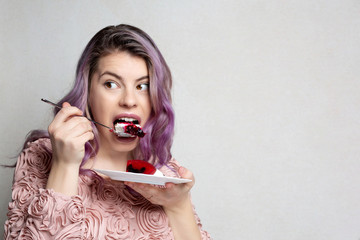 Greedy girl with purple hair eating yummy cheese cake over grey background. Empty space