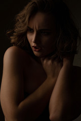 Angry brunette model with curly hair and naked shoulders posing with contrast light
