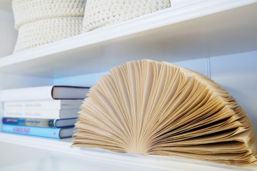 open book with pages lying on white bookshelf