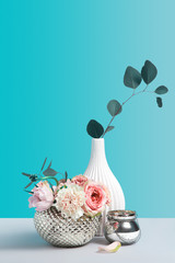 Rose flowers in metal stylish vase on grey table against color background. Flower shop concept with decor items. Minimalism still life composition with space for design.