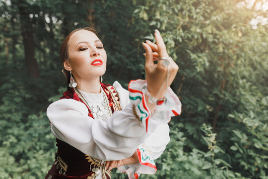A woman in traditional embroidered Turkic Eastern clothes performs a national dance in the Park