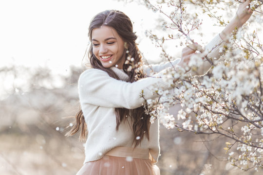 Pretty smiling teen girl are posing in garden near blossom cherry tree with white flowers. Spring time