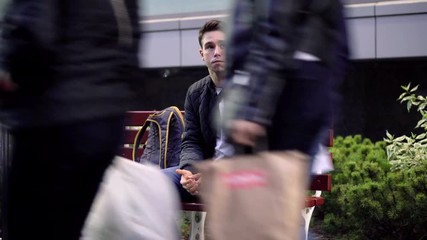 Young man sitting on bench in the street and waiting for something.