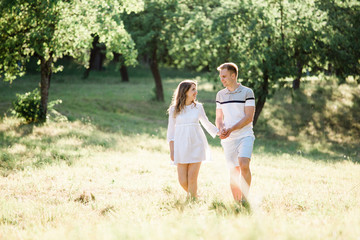 Young pretty couple in love walking  in park. Handsome cheerful blonde girl in white dress hugging her boyfriend. Man and woman having fun outdoors
