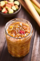 Homemade rhubarb jam in jar with raw rhubarb in the back (Selective Focus, Focus in the middle of the image)