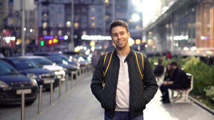 Young happy smiling man standing in the evening street with bokeh light effect