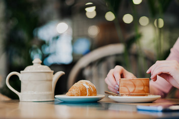 Breakfast in a cafe. Brown ceramic cup with tea and a croissant are on the table.