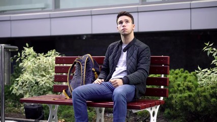 Young man sitting on bench in the street and waiting for something