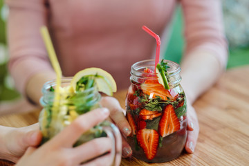 Close-up of the hands of two girls holding glass jars with red strawberry and yellow lemon lemonade.