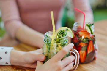 Close-up of the hands of two girls holding glass jars with red strawberry and yellow lemon lemonade.
