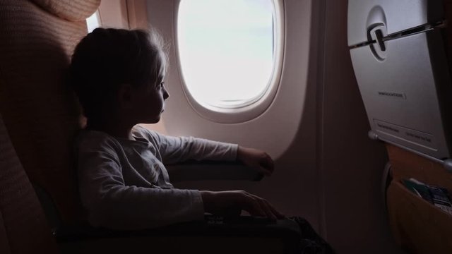 Cute girl with lollipop looking at the window in the airplane.