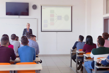 Female attractive professor explain lesson to students and interact with them in the classroom.Helping a students during class. University student being helped by female lecturer during class.