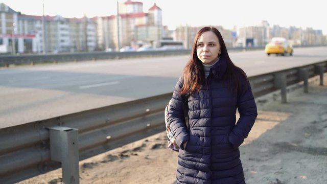Young woman on city roadside
Casual brunette in warm jacket standing on pavement of city roadway looking pensively away