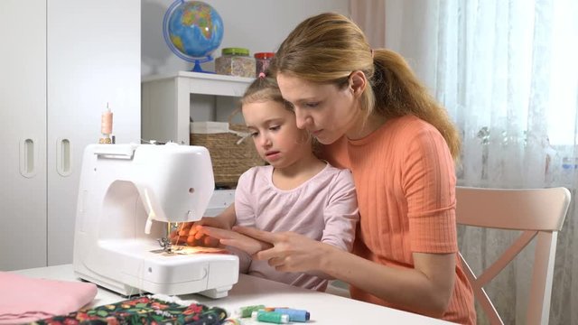Mother teaching her little daughter to sew using a sewing machine in the nursery at home. Children's craft, education and training
