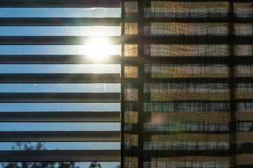 The sun shining through blinds, shades and a curtain. With a blue sky during springtime.
