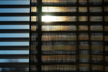 The sun shining through blinds, shades and a curtain. With a blue sky during springtime.