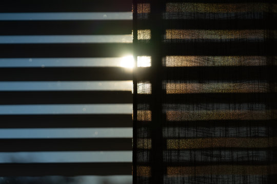 The sun shining through blinds, shades and a curtain. With a blue sky during springtime.