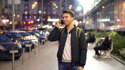 Young Attractive Man Speaking by Phone in the evening city street with bokeh light effect