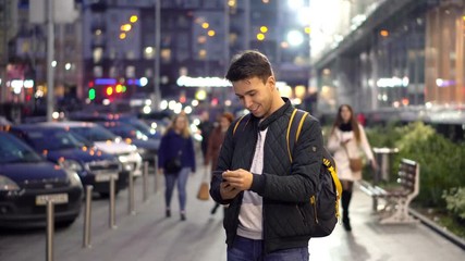 Young Attractive Man Using Smartphone in the evening city street with bokeh light effect.