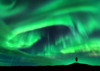 Obraz na płótnie Canvas Aurora borealis and silhouette of standing man. Lofoten islands, Norway. Aurora and happy man. Sky with stars and green polar lights. Night landscape with aurora and people. Concept. Travel background