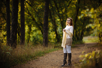 red-haired girl in bright clothes against a background of tree trunks in the autumn forest