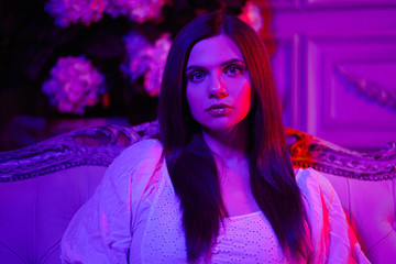 a beautiful girl in the light of a multi-colored light, on a chair with a soft rug, a gentle atmosphere in red-purple tones.