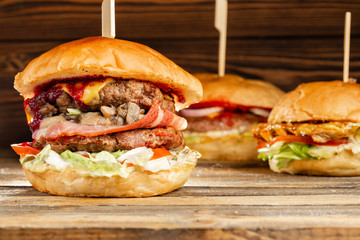 Three big burger with meat cooked on BBQ coal. Lunch on a wooden background. The concept of fast food and unhealthy food