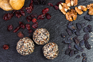 Theme sweet dessert made from natural products without sugar. Macro close-up of deserts ball round candy truffle on a black plate with natural dried fruit and seeds of white and black sesame and flax