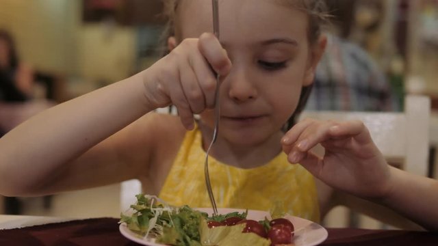 little girl eat green salad with appetite in the restaurant. Good health concept