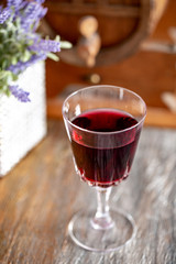 A glass of red wine and a bouquet of lavender flowers next to a wine wooden barrel. Art photography. Closeup. Soft focus.Toned image doesn’t in focus.