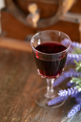 A glass of red wine and a bouquet of lavender flowers next to a wine wooden barrel. Art photography. Closeup. Soft focus.Toned image doesn’t in focus.