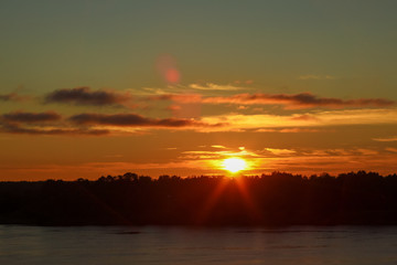 Naklejka premium Beautiful deep morning dawn with highlights in the orange rays of the summer sun on a river Volga with sun glare.. Toned in orange colour and backlit.