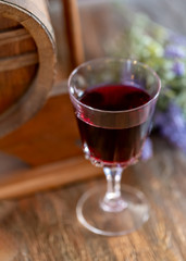 A glass of red wine and a bouquet of lavender flowers next to a wine wooden barrel. Art photography. Closeup. Soft focus.Toned image doesn’t in focus.