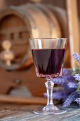 A glass of red wine and a bouquet of lavender flowers next to a wine wooden barrel. Art photography. Closeup. Soft focus.Toned image doesn’t in focus.