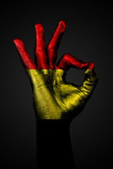 A hand with the painted flag of Belgium shows an OK sign on a dark background.