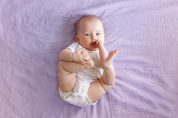 Portrait of cute adorable white Caucasian baby girl boy with blue eyes lying on bed looking at...
