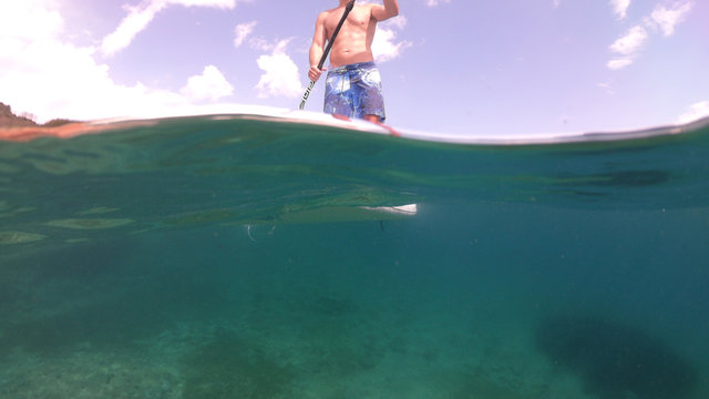 Underwater sea level photo of unidentified man in a paddle surf board known as Sup surfing in turquoise clear waters and beautiful blue cloudy sky