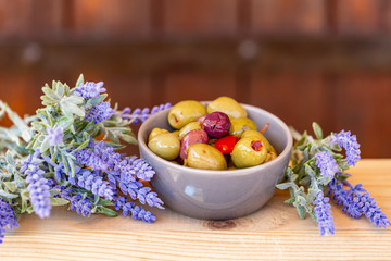 Olives stuffed with red pepper and herbs spices. Multi-colored olives in a small bowl on a wooden table. Lavender. Blurry background. Closeup. Soft focus. Copy space.