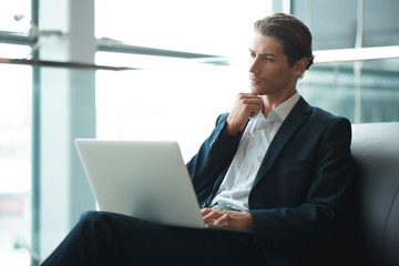 Fototapeta premium Young handsome man sitting in office with cup of coffee and working on project connected with modern cyber technologies. Businessman with notebook trying to keep deadline in digital marketing sphere.