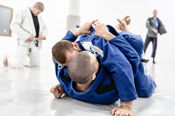 Two young BJJ Brazilian Jiu jitsu Athlete fighters training sparing technique at the academy fight lapel gi kimono