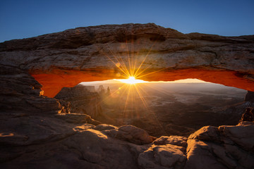 Mesa arch in Canyonlands National Park just outside Moab Utah. The sun beams like a sunstar through the window of the desert arch.  The cold snow contrasts the orange glow.