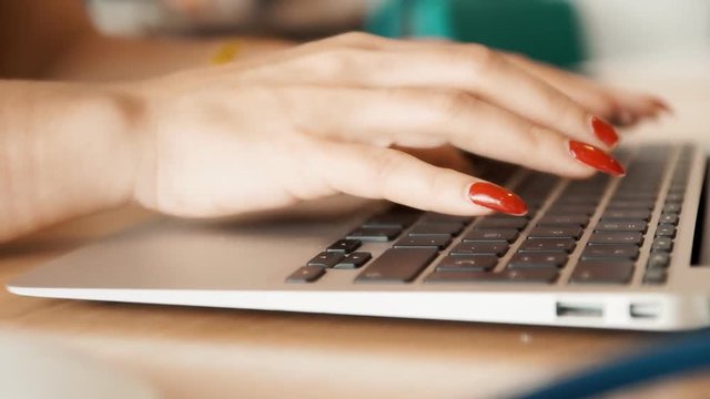 The hands of a woman typing on a laptop's keyboard. Long manicured nails with red polish. Handheld shot.