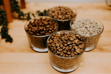 Glass Container Cups of Coffee Espresso Beans Roasted and Raw Green Beans on Wooden Product Display Table