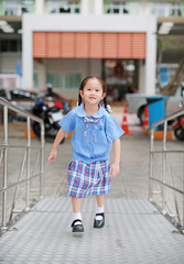 Happy little Asian child girl in school uniform running up metal stair.