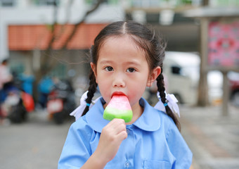 Portrait of little Asian child girl in school uniform eating ice cream.