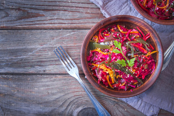 Dietary salad with sea kale, carrots, beets and sesame, sprinkled with olive oil in rustic ceramic bowl on wooden background. Detox concept